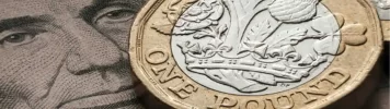 A close-up of a British one-pound coin resting on an image of Abraham Lincoln's face from a U.S. dollar bill