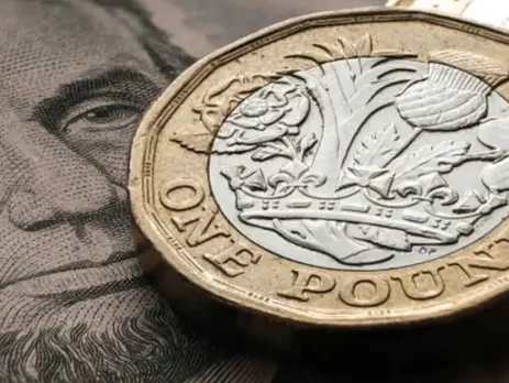 A close-up of a British one-pound coin resting on an image of Abraham Lincoln's face from a U.S. dollar bill