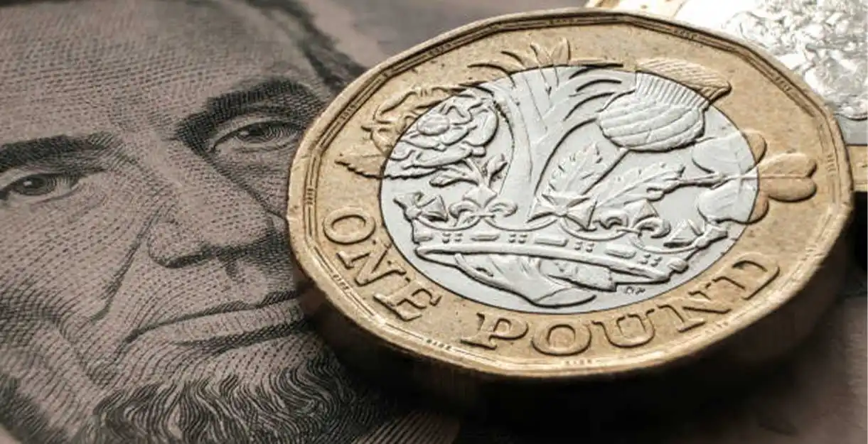 A close-up of a British one-pound coin resting on an image of Abraham Lincoln's face from a U.S. dollar bill