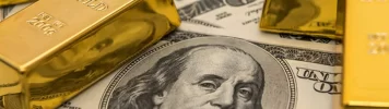 Several gold bars resting on top of 100-dollar bills, prominently featuring Benjamin Franklin's portrait